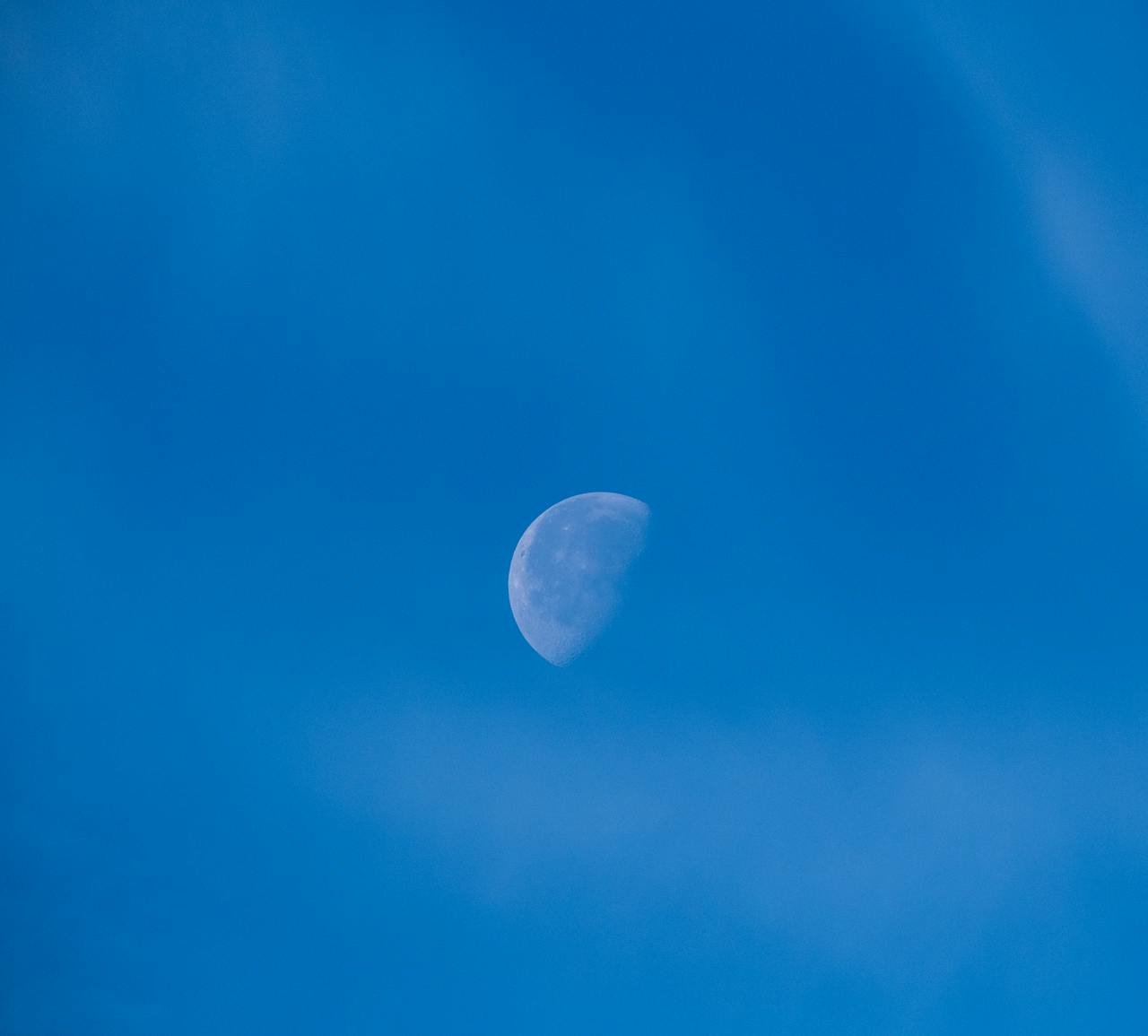 A half moon visible in a bright blue daytime sky over Bornova, İzmir, Türkiye.