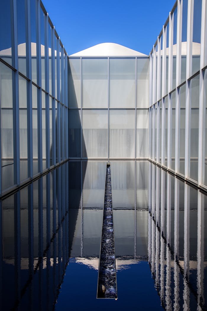 A contemporary building with glass facades reflecting water in an urban setting.