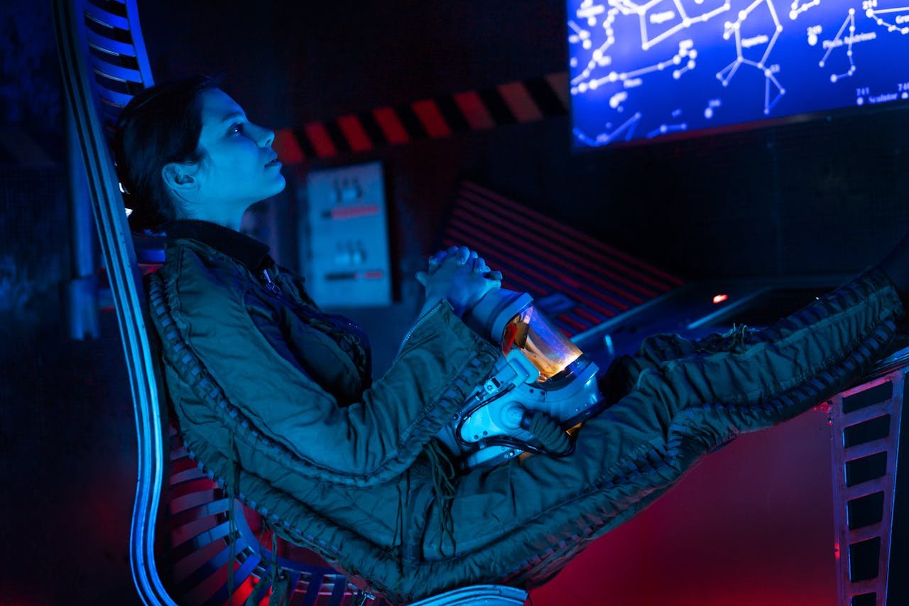 A woman in a spacesuit gazes at a futuristic screen, immersed in a blue glow.